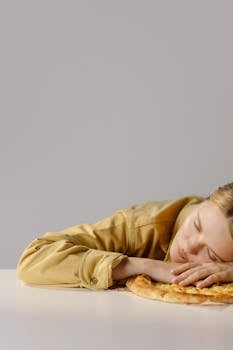 A Woman in Yellow Long Sleeves Sleeping beside a Pizza