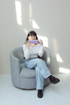 Woman in Denim Jeans and White Long Sleeve Sitting on Gray Sofa Chair